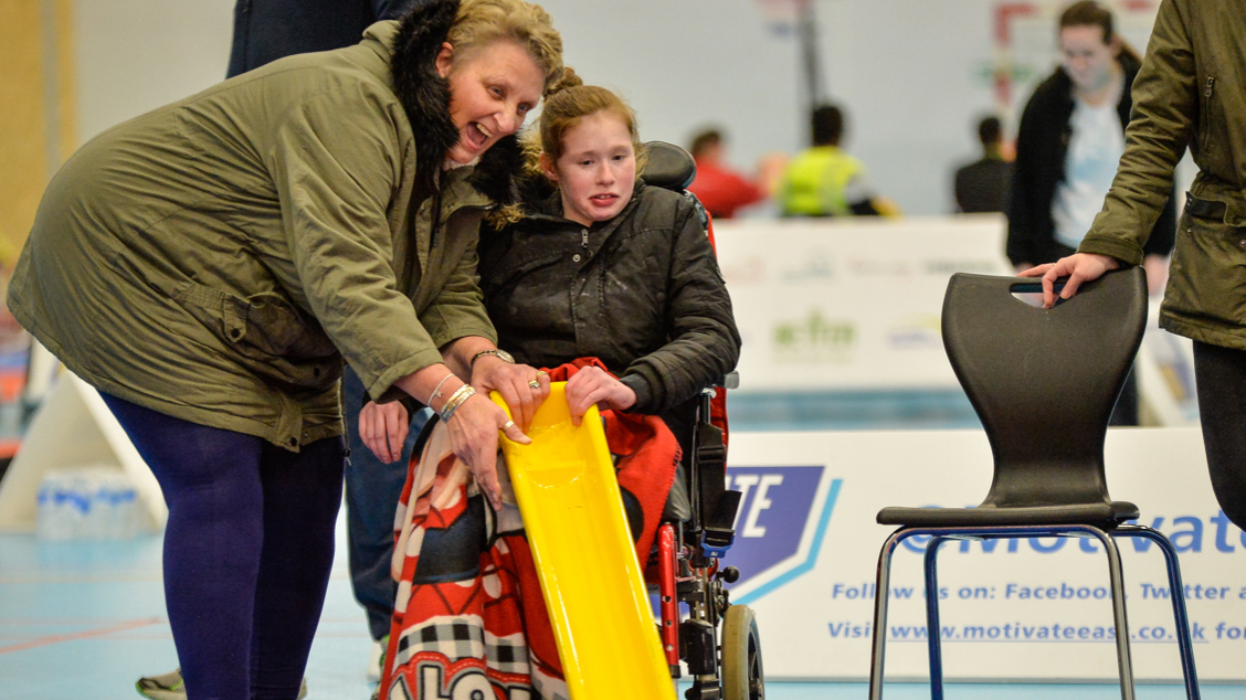 Girl, Wheelchair user, holding a yellow slide to roll a ball